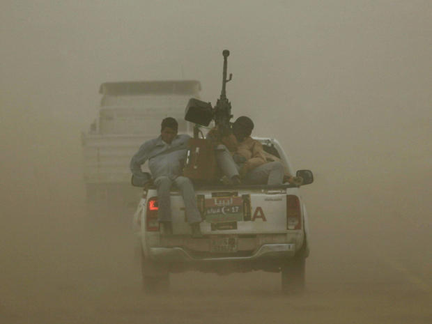 rebels riding at the back of an armed pickup truck brave a sand storm 