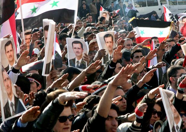 Syrian demonstrators raise posters showing Syria's President Bashar Assad 