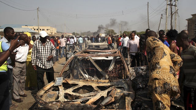 Onlookers stand by a destroyed car at the site of a bomb blast at St. Theresa Catholic Church in Madalla, Nigeria, Sunday, Dec. 25, 2011. An explosion ripped through a Catholic church during Christmas Mass near Nigeria's capital Sunday, killing at least 2 