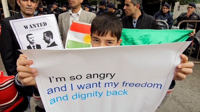 A Syrian Kurdish boy carries a banner during a protest outside the Arab League office in Beirut, Lebanon, Sunday, Dec. 25, 2011. The protesters said the Arab League was not serious in attempts to stop the Syrian regime crackdown. A man behind the boy was  