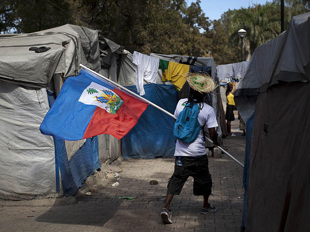 A demonstrator waves a Haitian flag while walking between makeshift tents at the temporary camp in Champ de Mars, across the street from the collapsed National Palace, during a protest to demand new housing in Port-au-Prince, Haiti, Jan. 11, 2012. 