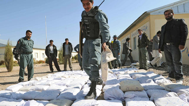 Afghan policemen stand next to packages containing opium 