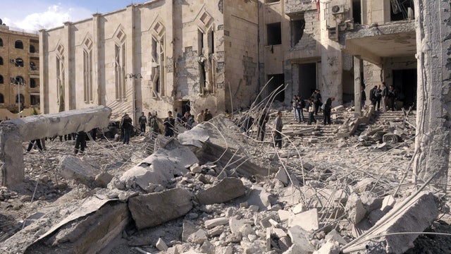 Syrian security forces walk on the wreckage of a damaged building 