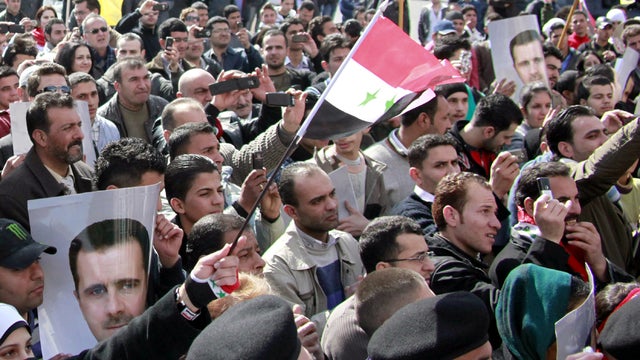 Syrian supporters of President Bashar al-Assad hold his portrait as they wave their national flag during a pro-regime demonstration at Sabe Bahrat Square in Damascus, Syria, Feb. 12, 2012. 