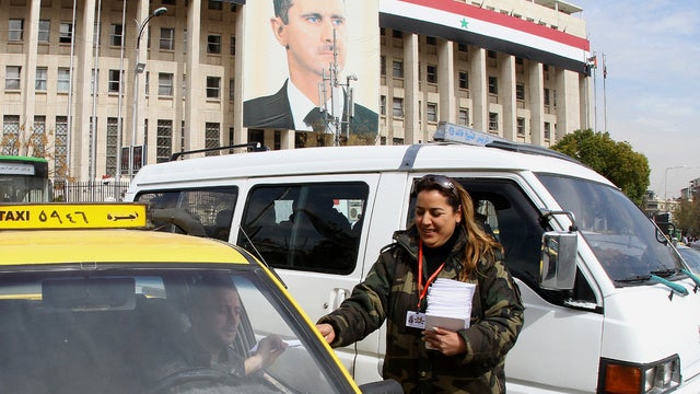 A woman hands a copy of the draft constitution to a taxi driver in Damascus 