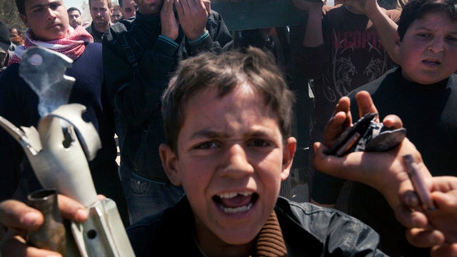 A Syrian boy holds the remains of mortar shells allegedly fired by the Syrian Army as mourners carry the coffin of 13-year-old Ahmad bin Muhsin Qarush during his funeral March 24, 2012, after he was said to have been killed two days earlier in shelling by 
