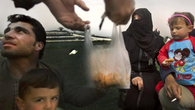 A member of the Free Syrian Army gives some food to a Syrian refugee family as they wait to cross to Turkey at the border between Syria and Turkey March 26, 2012. 