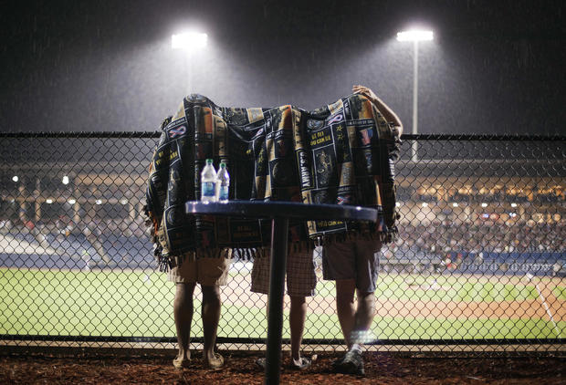 Fans take shelter under a blanket during a rain delay  