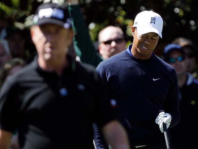 Miguel Angel Jimenez walks ahead of Tiger Woods as Woods reacts to his tee shot 