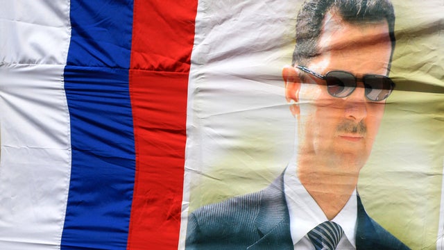 A portrait of Syrian President Bashar Assad hangs alongside the colors of the Russian flag during a pro-regime rally in Damascus, Syria, April 12, 2012, as a U.N.-backed cease-fire went into effect. 