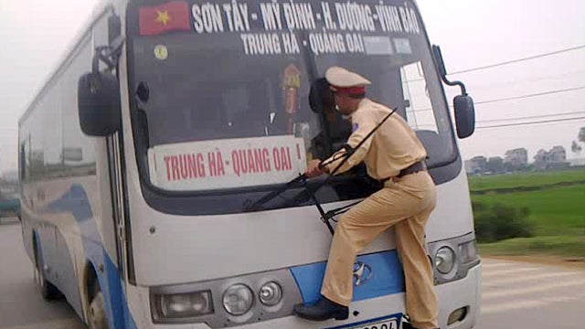 In this photo made from a video filmed Monday, April 9, 2012 and released by Hanoi Police, Vietnamese traffic police 2nd Lt. Nguyen Manh Phan clings on to the windshield wipers of a moving bus as he goes on a wild ride for nearly a kilometer  after the ro 