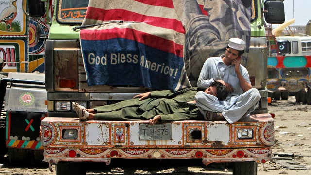 A Pakistani man speaks on his mobile phone on the bumper of oil tanker used to transport NATO fuel supplies to neighboring Afghanistan while another rests his head on his lap in Karachi, Pakistan, June 10, 2012. 