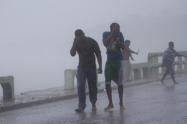 Local residents stay under the rain at the seafront of Enriquillo 