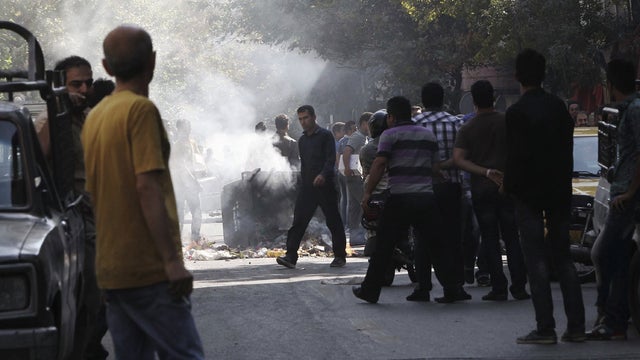 Iranians stand in a street as a garbage can is set on fire, in central Tehran, near Tehran's old main bazaar, on Wednesday, Oct. 3, 2012. 