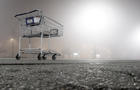 A shopping cart appears in an empty parking lot on a foggy night. 