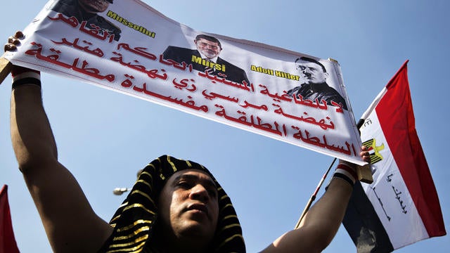 An Egyptian man dressed as a pharaoh holds a banner bearing a portrait of Egyptian President Mohammed Morsi flanked by portraits of Italian dictator Benito Mussolini and Adolf Hitler in Cairo's landmark Tahrir Square Nov. 30, 2012. 