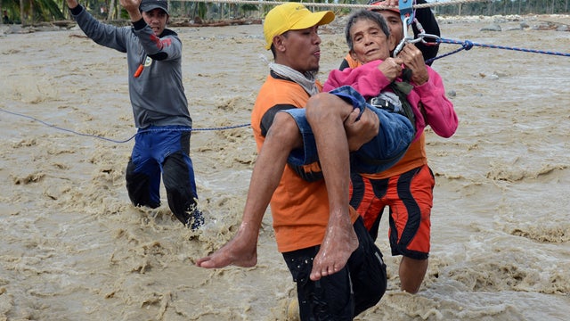 A rescue worker carries an elderly resident across a surging river in New Bataan 