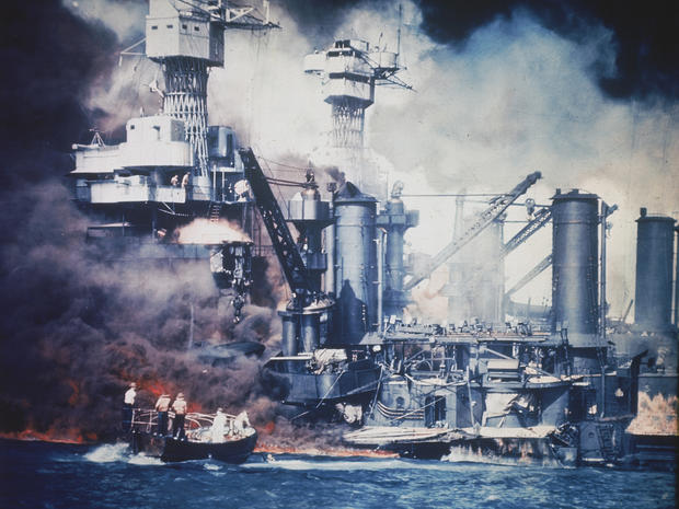 In this U.S. Navy file photo, a small boat rescues a USS West Virginia crew member from the water after the Japanese bombing of Pearl Harbor, Hawaii on Dec. 7, 1941 during World War II. Two men can be seen on the superstructure, upper center. The mast of  