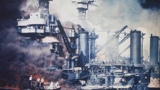 In this U.S. Navy file photo, a small boat rescues a USS West Virginia crew member from the water after the Japanese bombing of Pearl Harbor, Hawaii on Dec. 7, 1941 during World War II. Two men can be seen on the superstructure, upper center. The mast of  