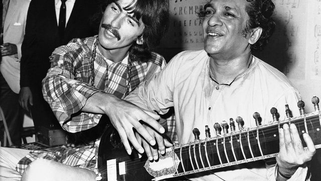 Aug. 3, 1967 file photo shows George Harrison, of the Beatles, left, sitting cross-legged with his musical mentor, Ravi Shankar, of India, in Los Angeles, as Harrison explains to newsmen that Shankar is teaching him to play the sitar 