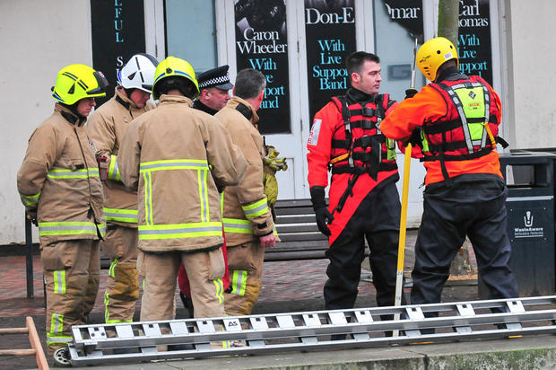 Members of the Hertfordshire Fire and Rescue service stand next to the village pond in Watford 