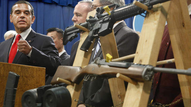 Los Angeles Mayor Antonio Villaraigosa, left, glances over to pair of semi-automatic rifles as he discusses his support for proposed gun control legislation at news conference in Sacramento, Calif., Feb. 7, 2013. 