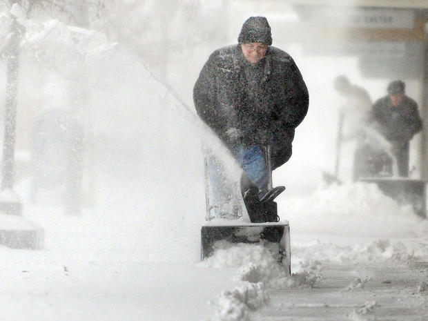 Chuck Carroll, center, uses a snowblower to clear the sidewalk in front of his business in downtown Salina, Kan., Feb. 21, 2013. 