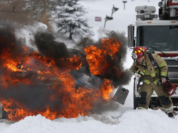 A firefighter places wheelblocks as he prepares to extinguish a vehicle fire in Lawrence, Kan., Feb. 21, 2013. The car caught on fire trying to make it up a snow covered hill. 