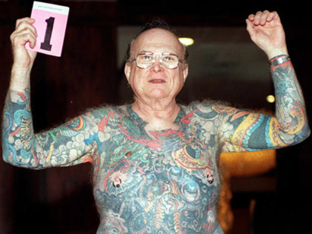 Larry Happ, 68, raises his arms to show his tattoo 
