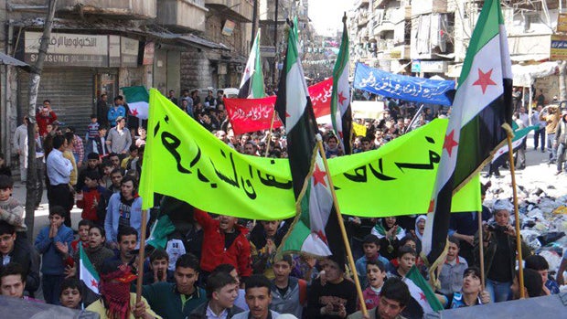 This citizen journalism image provided by The Syrian Revolution which has been authenticated based on its contents and other AP reporting, shows anti-Syrian regime protesters holding banners and Syrian revolution flags, during a demonstration in the neigh 