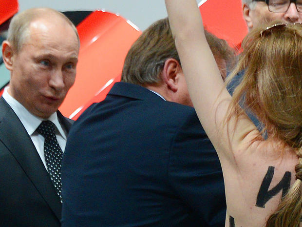 A topless demonstrator with written messages on her back walks towards Russian President Vladimir Putin , left and German Chancellor Angela Merkel, right, during the opening tour at the Hannover Fair in Hannover, Germany, Monday April 8, 2013.  