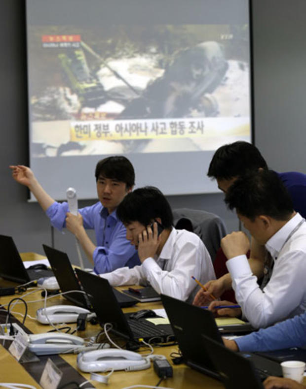 Employees of Asiana Airlines talk on phones near a screen showing a news program reporting about Asiana Airlines flight 214 which took off from Seoul and crashed while landing at San Francisco International Airport at the Crisis Management Center of Asian 