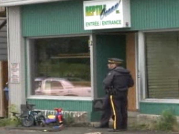 Police stand in front of Reptile Ocean pet store in New Brunswick, Canada on Aug. 5, 2013, after two young boys were strangled as they slept by a python that escaped the store and apparently slithered through the ventilation system into the apartment above. Their tricycles can be seen at bottom left. 