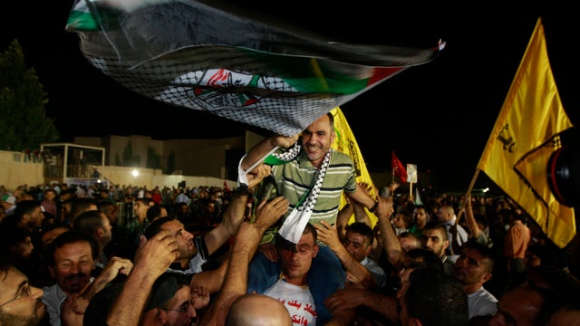 A released Palestinian prisoner Esmat Mansour, center, waves a flag as he is cheered at the Palestinian Authority headquarters in the West Bank city of Ramallah, Aug. 14 , 2013. 