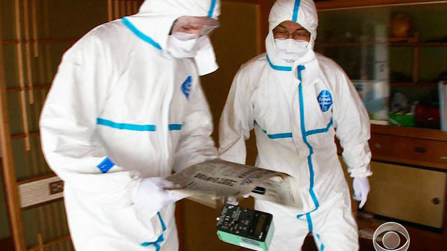 Akira Okawara and Seth Doane wear protective suits to travel to Okuma. 