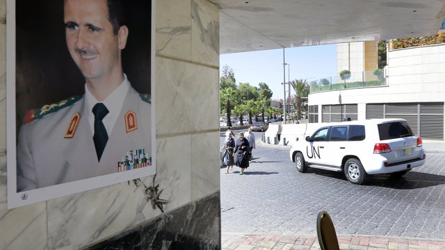 A poster of Syrian President Bashar Assad adorns a wall as a United Nations vehicle carrying inspectors from the OPCW leaves a hotel in Damascus 