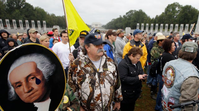 Noreen Grimm stands next to her husband David Grimm, both from Pittsburgh, Pa., holding a portrait of President George Washington during a rally at the World War II Memorial in Washington Sunday, Oct. 13, 2013.  