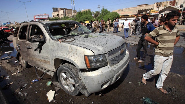 People and security forces inspect the site of a car bomb attack in Basra 