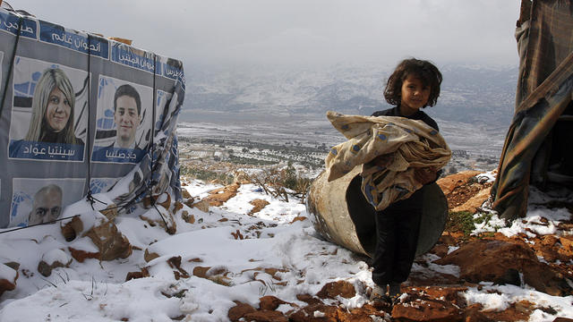 A young Syrian refugee carries a blanket next to a tent in a makeshift refugee camp in the Lebanese village of Qaraoun, in the Bekaa Valley 