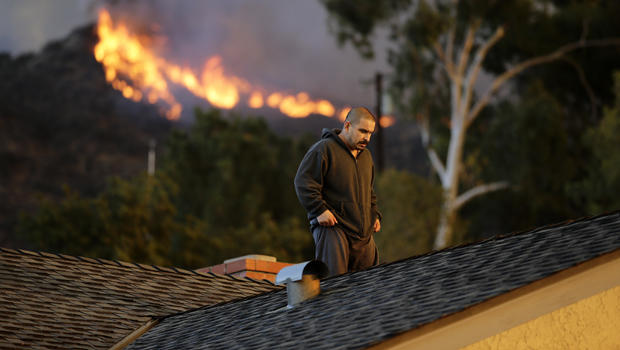 A man walks off a rooftop after spraying water on his home as firefighters battle a wildfire Jan. 16, 2014, in Azusa, Calif. 