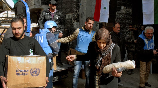 Palestinian residents of the besieged refugee camp of Yarmouk carry supplies given to them by the United Nations at the gate of the camp 