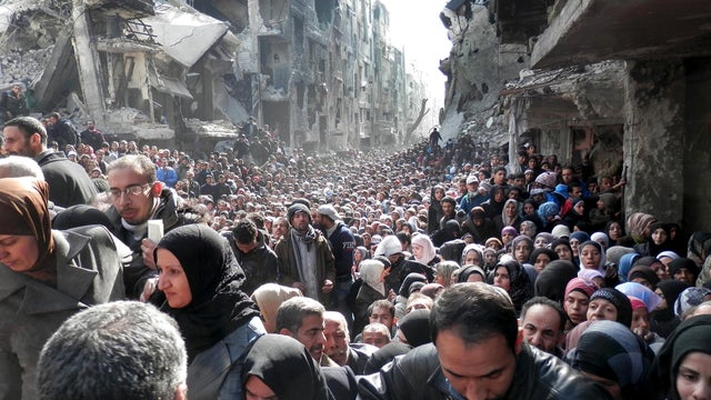 Residents of the besieged Palestinian camp of Yarmouk line up to receive food supplies in Damascus 
