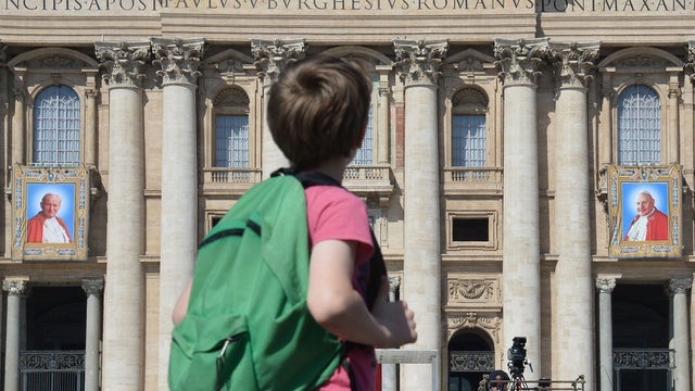 A boy looks towards tapestries showing portraits of late Popes John Paul II (L) and John XXIII on the balconies of St. Peter's basilica 