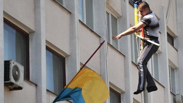 A pro-Russian activist throws down Ukrainian flag as he climbed up on the flagpole outside the state city building in southern Ukrainian city of Mariupol as Ukrainian police left guarding the building 