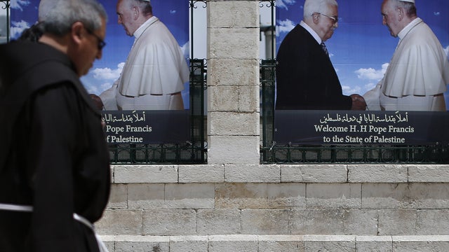 Two Franciscan priests walk past banners bearing portraits of Pope Francis and Palestinian President Mahmud Abbas near the Church of Nativity in the West Bank Town of Bethlehem 