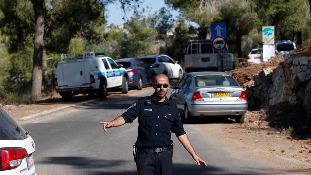 An Israeli police officer gestures in the Jerusalem Forest, where a body was found an hour after police received a call saying a young Palestinian boy had been abducted 