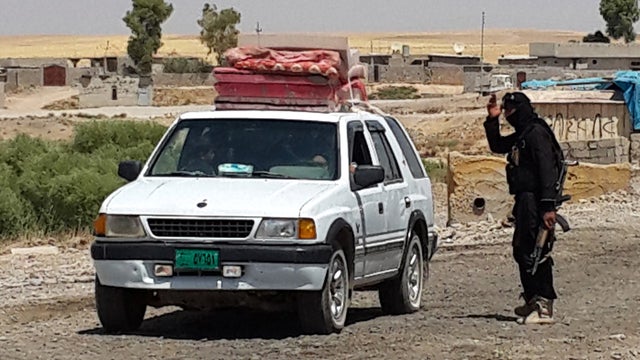 A fighter with ISIS directs a vehicle with a Christian family to leave from their home village outside Erbil 