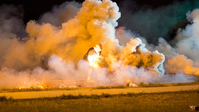 ​A protester throws back a smoke bomb while clashing with police in Ferguson, Missouri, Aug. 13, 2014. 
