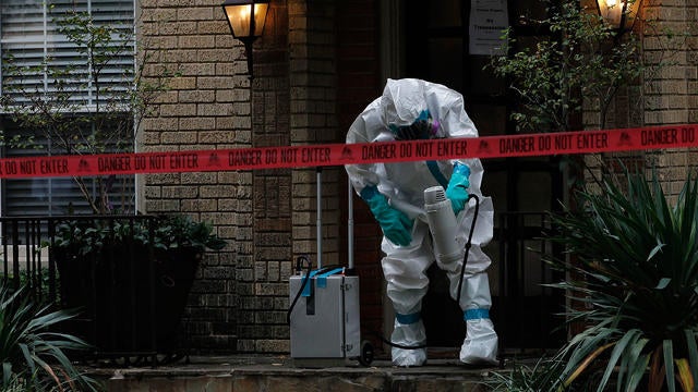 A man dressed in protective hazmat clothing treats the front porch of an apartment where a second person diagnosed with the Ebola virus resides 