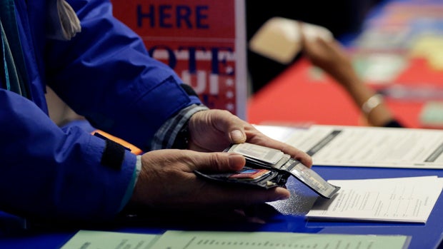 A voter shows his photo identification to an election official at an early voting polling site in Austin, Texas, Feb. 26, 2014. 
